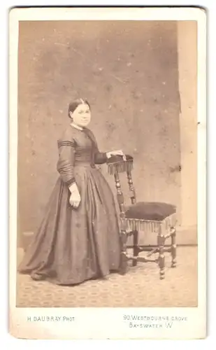 Fotografie H. Daubray, Bayswater, Westbourne Grove 90, Portrait junge Frau im Biedermeierkleid neben einem Stuhl