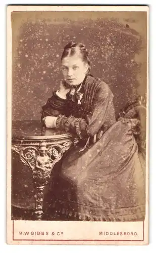Fotografie R. W. Gibbs & Co., Middlesboro, Wilson Street 220, Portrait Dame im Biedermeierkleid auf einen Tisch gelehnt