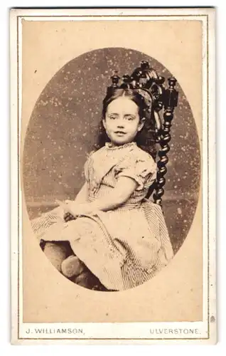 Fotografie J. Williamson, Ulverstone, Portrait Mädchen im gestreiften Kleid auf einem Stuhl sitzend