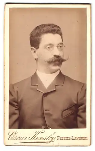 Fotografie Oscar Kensky, Neisse-Landeck, Portrait Herr im Anzug mit voluminösem Oberlippenbart und Brille