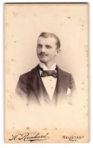 Fotografie H. Reinhard, Neustadt a. H., Portrait junger Mann im feinen Anzug mit Fliege und Kaiser Wilhelm Bart