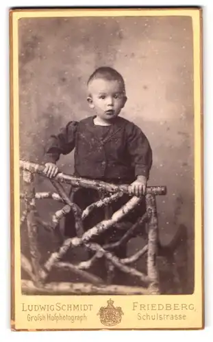 Fotografie Ludwig Schmidt, Friedberg, Schulstrasse 357, Kleiner Junge im dunklen Kleid neben einem Holzgerüst