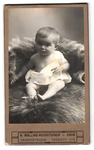 Fotografie H. Malling-Rechsteiner, Chur, Grabenstr., Portrait Kleinkind im Leibchen auf einem Fell