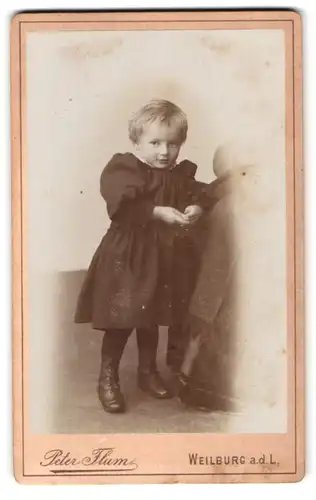 Fotografie Peter Flum, Weilburg a. d. L., Portrait Kleinkind im Kleid mit verschmitzten Blick