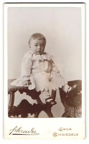 Fotografie Schrader, Chur, Poststr., Portrait Kleinkind im weissen Wollkleid mit Topfhaarschnitt