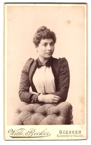 Fotografie Wilh. Becker, Giessen, Bahnhofstr., Portrait junge Frau im Kleid mit Locken lehnt an einem Sessel