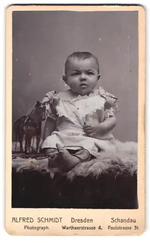 Fotografie Alfred Schmidt, Dresden, Warthaerstr. 4, Portrait niedliches Baby im Schleifenkleidchen auf Fell sitzend