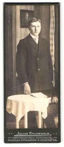 Fotografie Julius Grunewald, Oberneukirch, charmanter junger Mann im Anzug am Tisch stehend