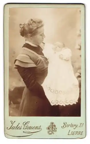Fotografie Jules Geuens, Lierre, Berlary 31, Portrait stolze junger Mutter hält Baby im Taufkleidchen im Arm