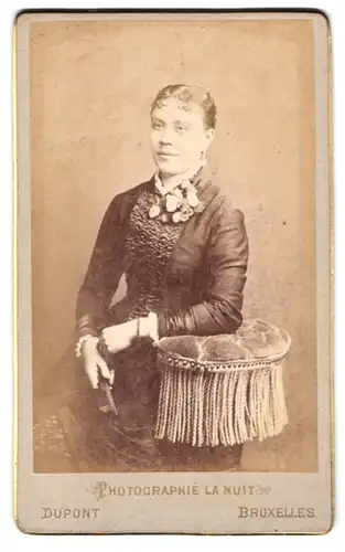 Fotografie Dupont, Bruxelles, 67 Rue Neuve, Portrait einer elegant gekleideten jungen Frau mit Ansteckblumen am Kleid