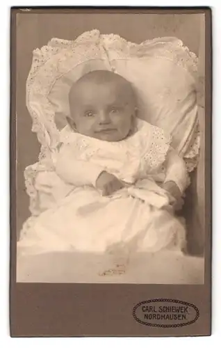 Fotografie Carl Schiewek, Nordhausen, Töpferstrasse 1, amüsiert wirkendes Baby in weissem Spitzenkleidchen