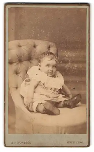 Fotografie A. H. Vorbeck, Holsterbro, Kleinkind mit struwweligem Haar auf Sessel