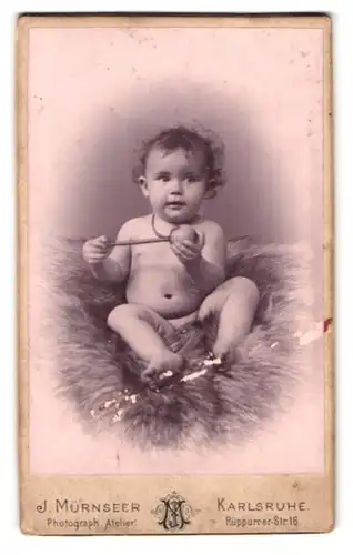 Fotografie J. Mürnseer, Karlsruhe, Rüppurrer-Str. 16, Portrait nacktes kleines Kind mit Locken und Rassel in der Hand