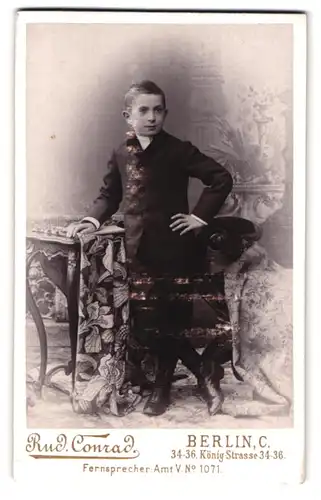 Fotografie Rud. Conrad, Berlin, König-Str. 34-36, Portrait junger Knabe im Anzug lehnt am Tisch