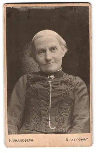 Fotografie H. Brandseph, Stuttgart, Marienstrasse 36, lächelnde ältere Dame in schwarzen Kleid mit Kragenbrosche