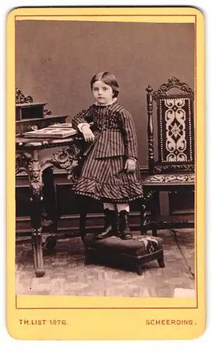 Fotografie Th. List, Scheerding a. Inn, Portrait Mädchen im gestreiften Kleid steht auf einem Hocker