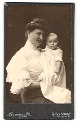 Fotografie Leverin & Co., Stockholm, Drottninggatan 61, Portrait Mutter in weisser Bluse zeigt stolz ihr kleines Kind