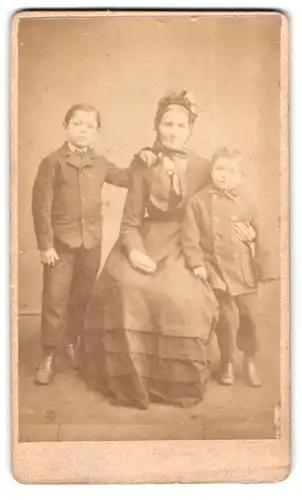 Fotografie Fotograf und Ort unbekannt, Portrait Oma mit zwei Enkelkindern in Anzügen