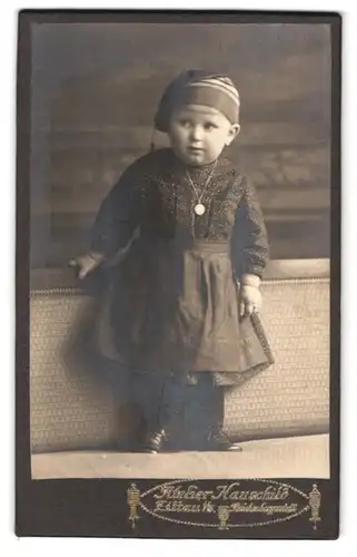 Fotografie Atelier Hauschild, Zittau i. S., Portrait Kleinkind im Pünktchenkleid mit Mütze