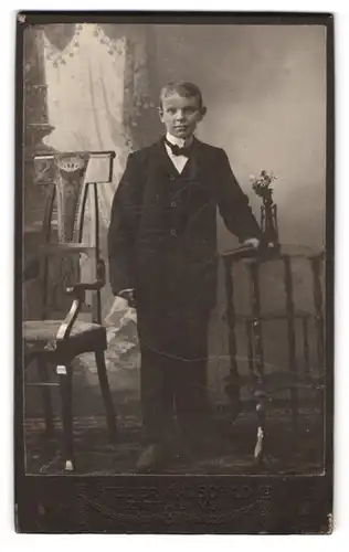 Fotografie Herm. Hauschild, Zittau, Cirkus-Allee 4, Portrait Junge im Anzug mit Fliege vor einer Studiokulisse