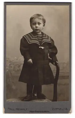 Fotografie Paul Heinelt, Zittau i. S., Bautznerstr. 18, Portrait Kleinkind im Kleid steht auf einem Stuhl