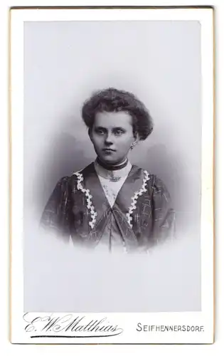 Fotografie E. W. Matthias, Seifhennersdorf, Portrait junge Frau im gemusterten Kleid mit Brosche und toupirten Haaren