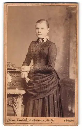 Fotografie Herm. Neudeck, Uelzen, Gudesstr. 180, Portrait junge Frau im Biedermeierkleid mit Brosche lehnt am Tisch