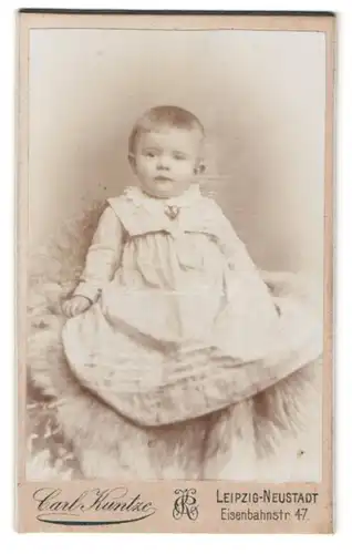 Fotografie Carl Kuntze, Leipzig, Eisenbahnstr. 47, Portrait kleines Kind im Kleid auf einem Fell sitzend