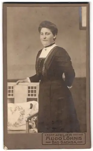 Fotografie Hugo Löhnis, Bad Sachsa, Portrait Dame im Biedermeierkleid mit Brosche steht an einem Stuhl
