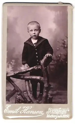 Fotografie Emil Hansen, Svendborg, Mollergade 50, Portrait frecher blonder Bube im Anzug am Geländer stehend