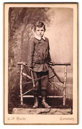 Fotografie C. F. Halm, Constanz, Rosgartenstr. 20, Portrait frecher Bube im Anzug am Holzgeländer stehend