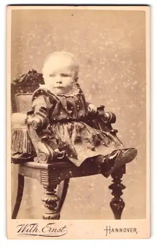 Fotografie Wilh. Ernst, Hannover, Angerstrasse 13a, Portrait Kleinkind im Kleid sitzt im Kinderstuhl