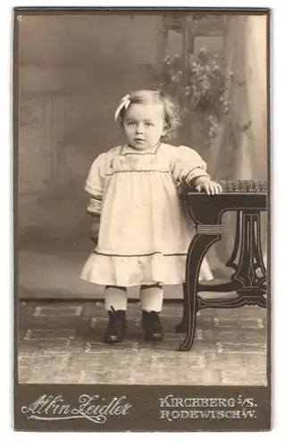 Fotografie Albin Zeidler, Kirchberg i. S., Neumarkt 238, Portrait kleines Mädchen im weissen Kleid mit Haarschleife