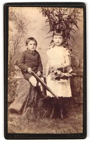 Fotografie A. Drawe, Berlin, Münz-Str. 7, Portrait Bruder und Schwester mit Gewehr und Blumenkorb vor Studiokulisse