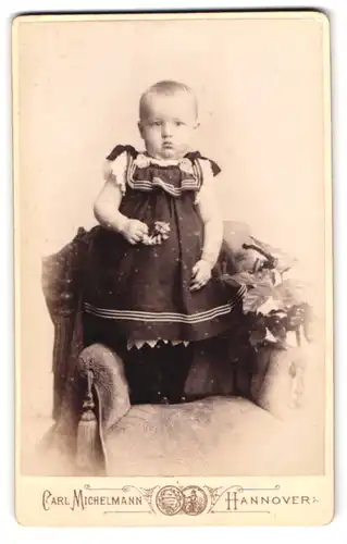 Fotografie Carl Michelmann, Hannover, Ständehausstr. 2, Baby im Kleid auf Sessel stehend