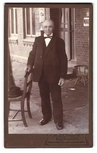 Fotografie H. Behning, Buxtehude, betagter Herr im Anzug vor einem Lebensmittelgeschäft