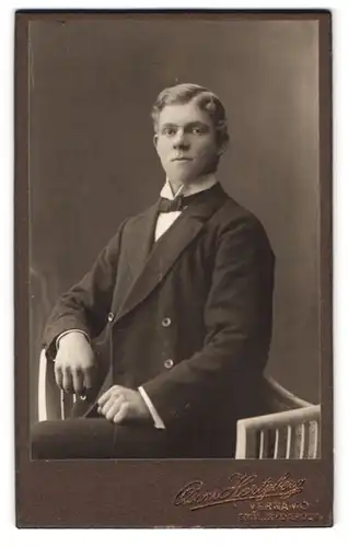 Fotografie Oscar Hertzbergs, Vernamo, Portrait junger Mann im Anzug mit Fliege sitzt gerade im Atelier