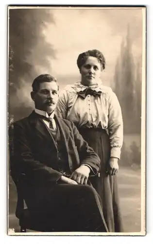 Fotografie Fotograf und Ort unbekannt, Portrait Paar im Anzug und Kleid vor einer Studiokulisse