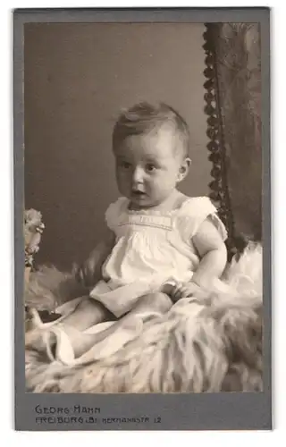 Fotografie Georg Hahn, Freiburg i. B., Hermannstrasse 12, verblüfftes Kleinkind auf Schafsfell