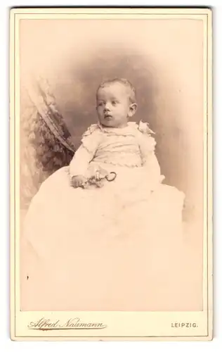 Fotografie Alfred Naumann, Leipzig, Dorotheenstrasse, Portrait Kleinkind im langen weissen Kleid mit Rassel in der Hand