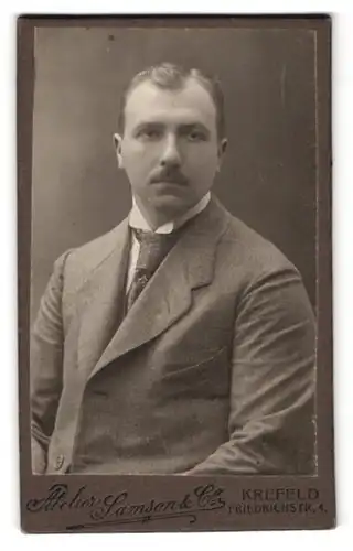 Fotografie Samson & Co., Krefeld, Friedrichstrasse 4, Portrait Mann im grauen Anzug mit Krawatte schaut trocken