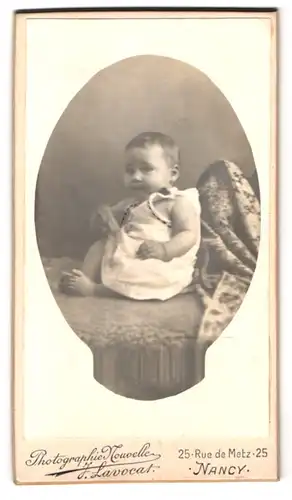Fotografie J. Lavocat, Nancy, Rue de Metz 25, Portrait kleines Kind im weissen Kleid auf einem Sofoa sitzend