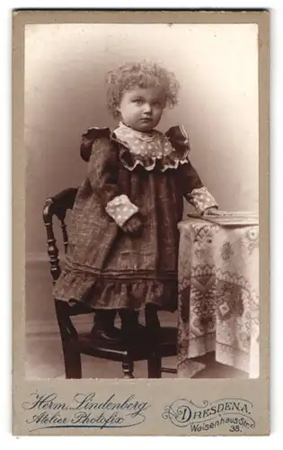 Fotografie Herm. Lindenberg, Dresden, Waisenhausstr. 38, Portrait kleines Mädchen im Kleid mit Locken steht auf Stuhl