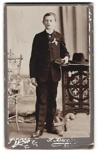 Fotografie Fotograf und Ort unbekannt, Portrait junger Knabe im Anzug mit Hut und Ansteckschleife