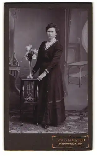 Fotografie Emil Wolster, Finsterwalde, Schulstrasse, gut gekleidete Dame in schwarzem Kleid mit Blumenvase