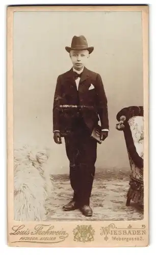 Fotografie Louis Frohwein, Wiesbaden, Webergasse 2, Portrait junger Knabe im Anzug mit Hut und Lederhandschuhen