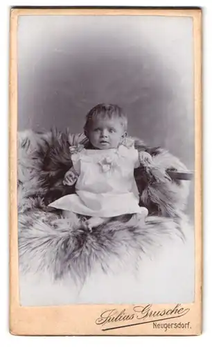 Fotografie Julius Grusche, Neugersdorf i. S., Baby im Kleidchen auf Felldecke liegend