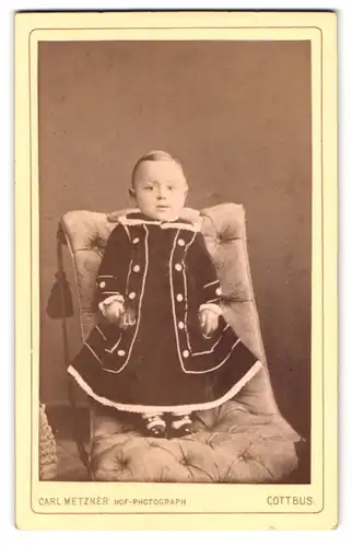 Fotografie Carl Metzner, Cottbus, Schlosskirchplatz 27b, Kleinkind im Kleidchen auf Sessel stehend