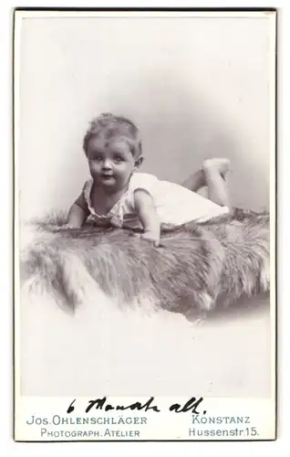 Fotografie Jos. Ohlenschläger, Konstanz, Hussenstr. 15, Portrait Kleinkind im Leibchen auf einem Fell liegend