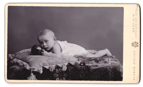 Fotografie Globus Atelier, Berlin, Leipziger Str. 132 /135, Portrait Kleinkind im weissen Kleid mit Ball auf einem Kissen